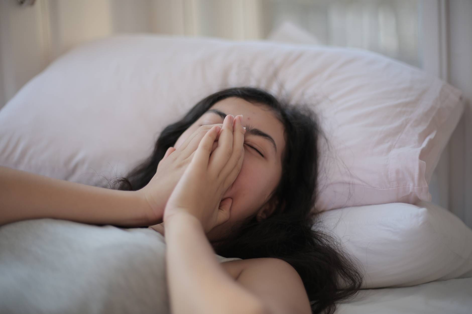 woman lying on bed covering her face with her hands