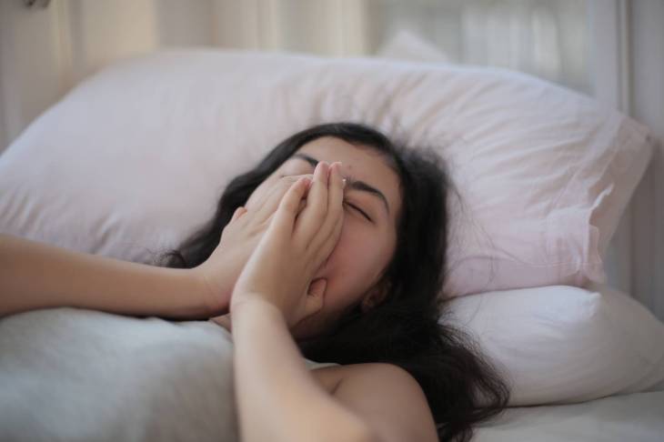woman lying on bed covering her face with her hands